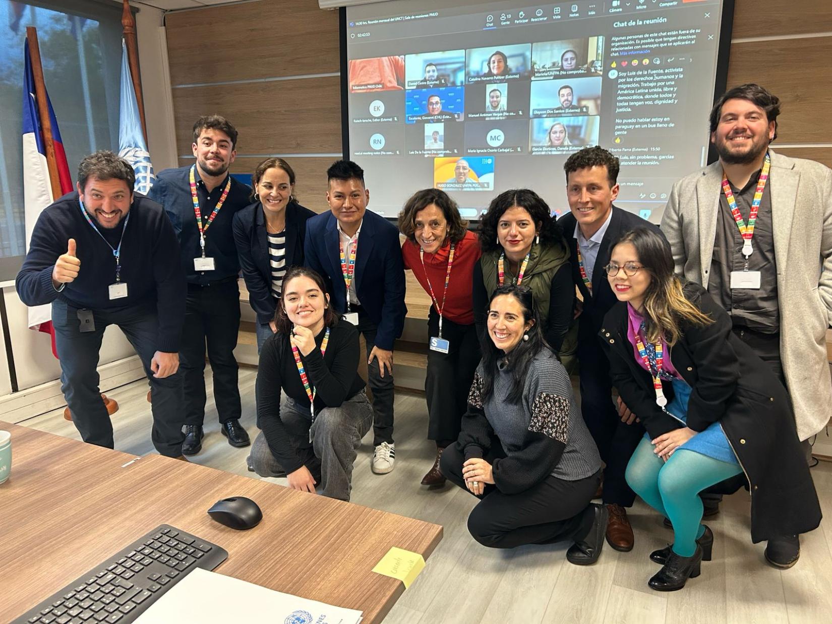 Foto de grupo de personas, algunas paradas y otras en cuclillas, en una sala de reuniones. Las personas de la foto corresponden a miembros del Grupo de Referencia de Jóvenes y representantes del Equipo País de ONU Chile